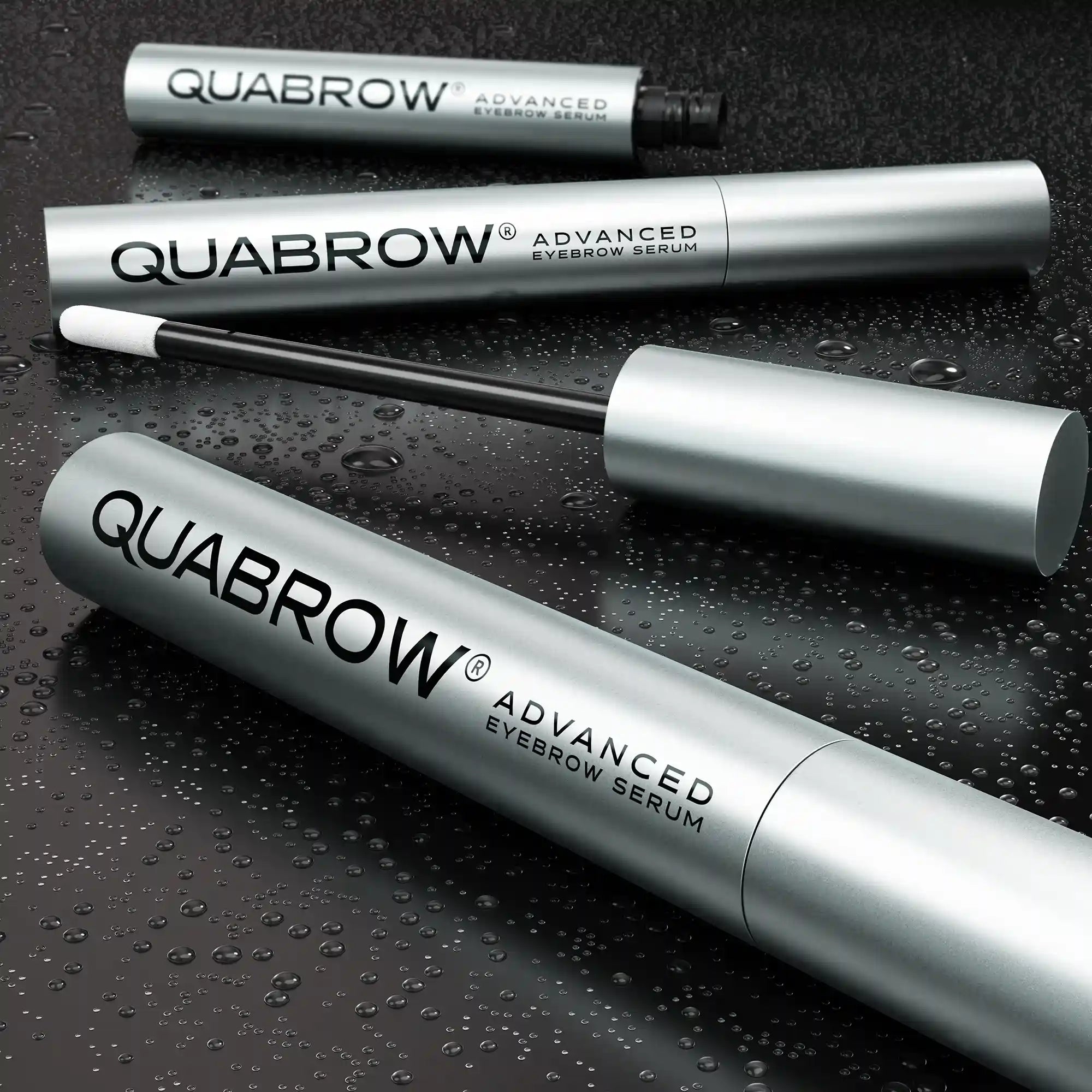 QUABROW Eyebrow Serum DUO SET displayed on wet dark surface with open applicator and water droplets